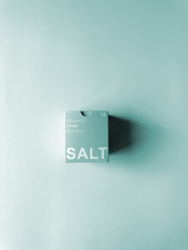 Artistic shadow play on the minimalist sea green packaging of UMAMI SEA SALT TYPE °02 UNNUR, subtly emphasizing ‘SALT’ for its refined salt with seaweed.